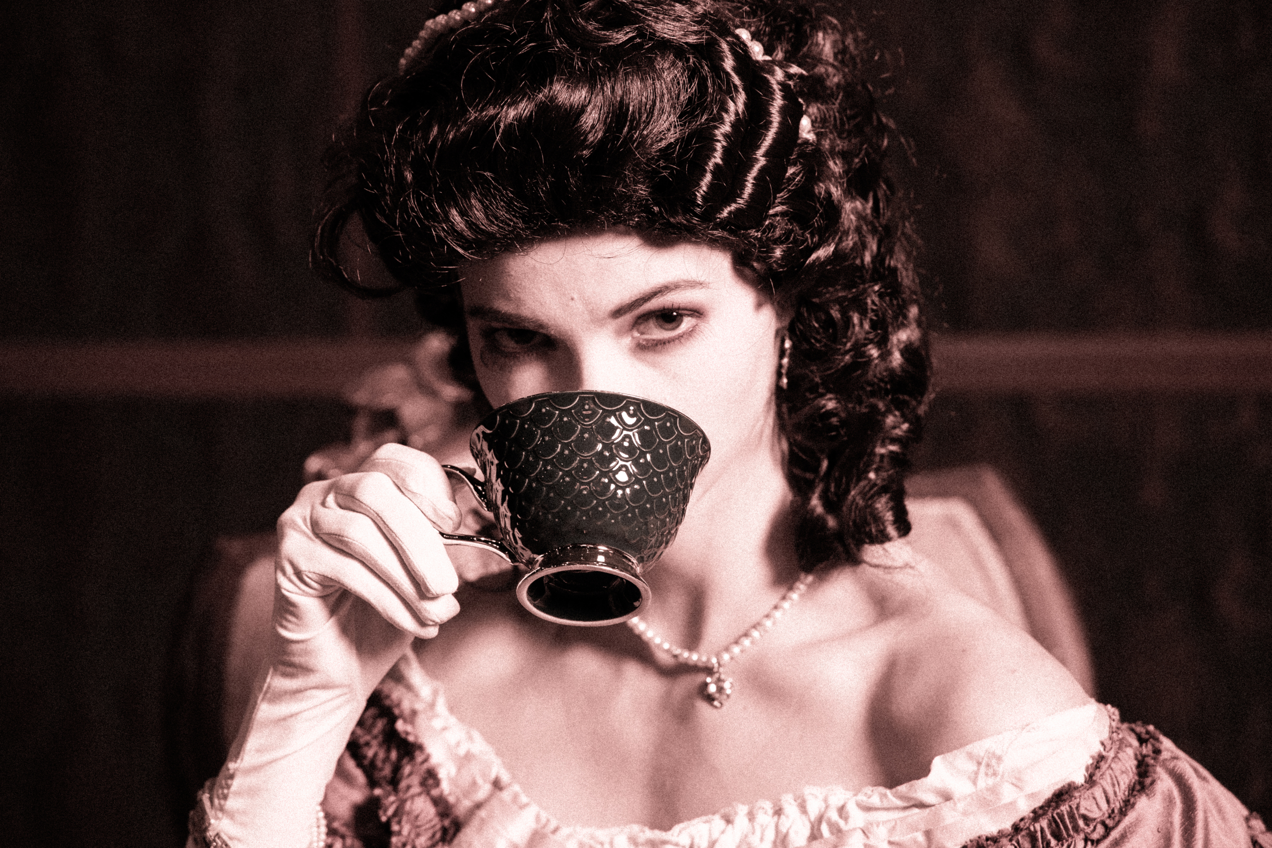 A quiet moment steeped in elegance where vintage glamour meets timeless intrigue as she lifts a delicate teacup, her gaze as rich as the shadows around her.