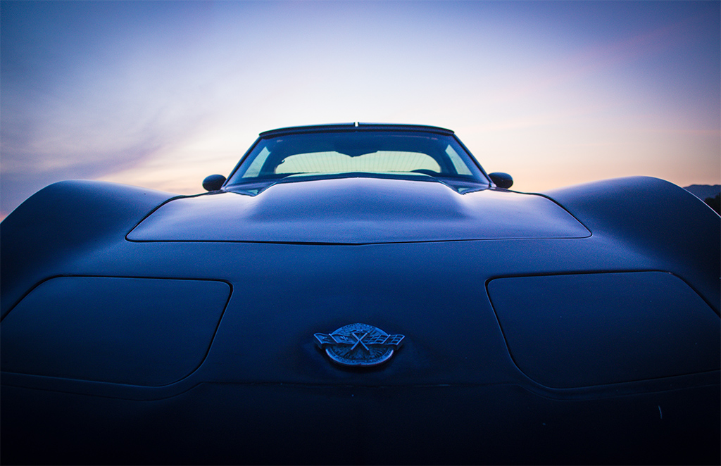 A bold front view of a classic sports car, its sculpted curves and iconic emblem framed by the soft glow of dusk.