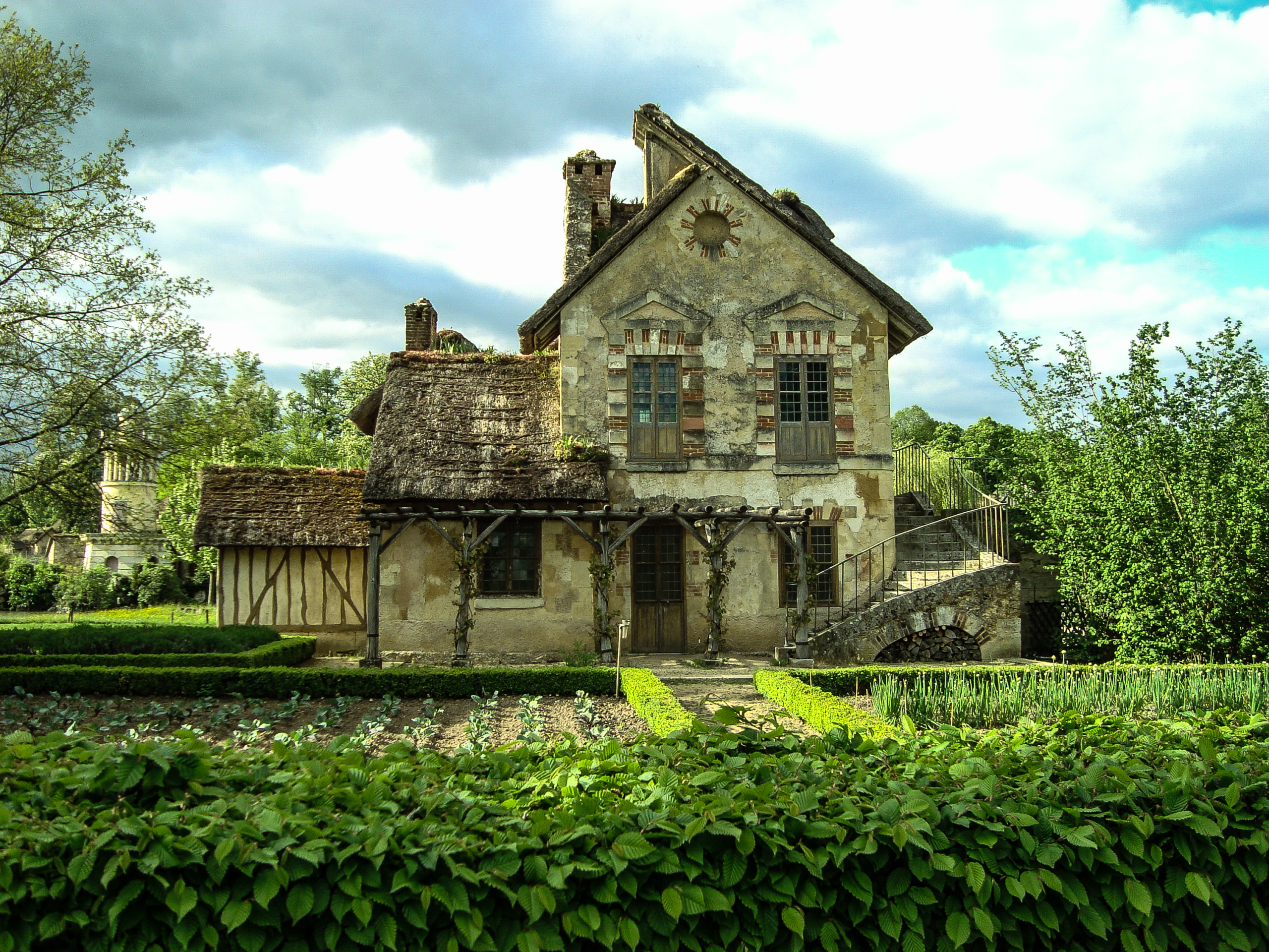 A storybook cottage nestled among manicured gardens, where weathered stone, timber beams, and vibrant greenery come together in quiet countryside charm.